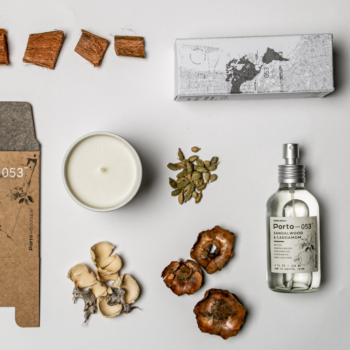 Porto-053 room spray and box in a flat lay with a candle, cardamom and dried flowers