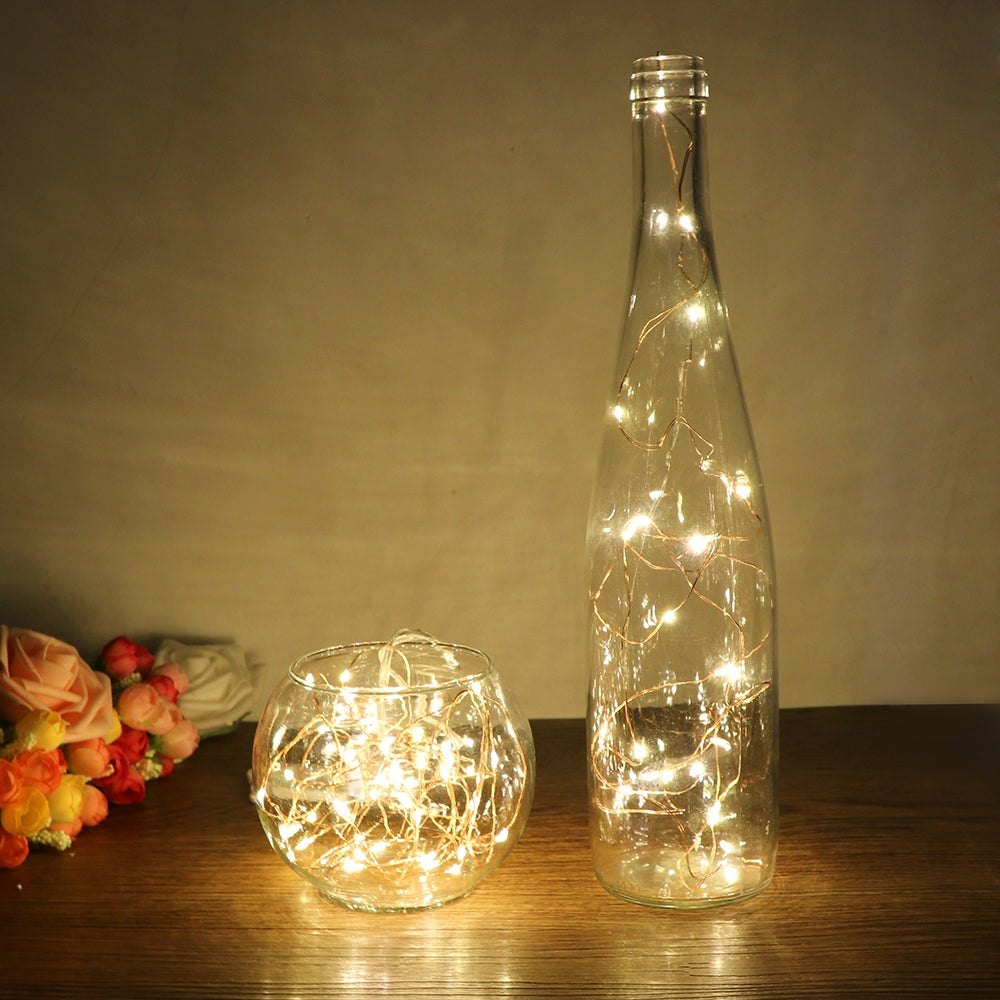 Copper wire fairy lights glowing inside a glass bottle and a glass bowl
