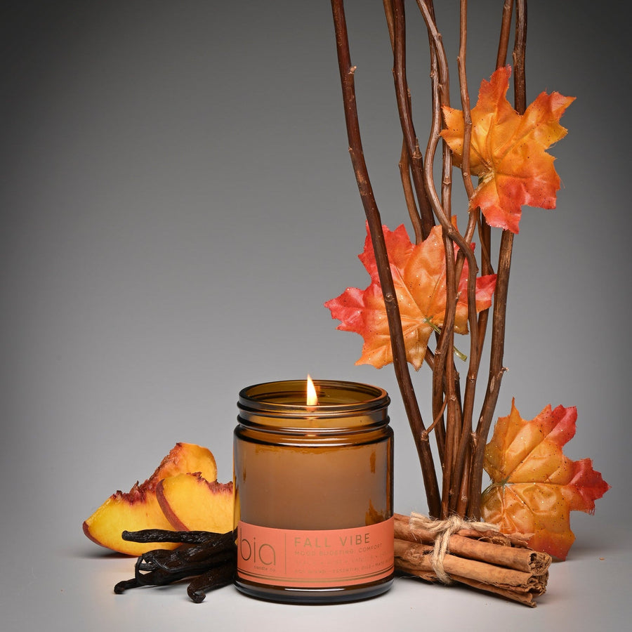 Lit Fall Vibe candle in an amber jar with autumn branches, peach slices, cinnamon sticks and vanilla
