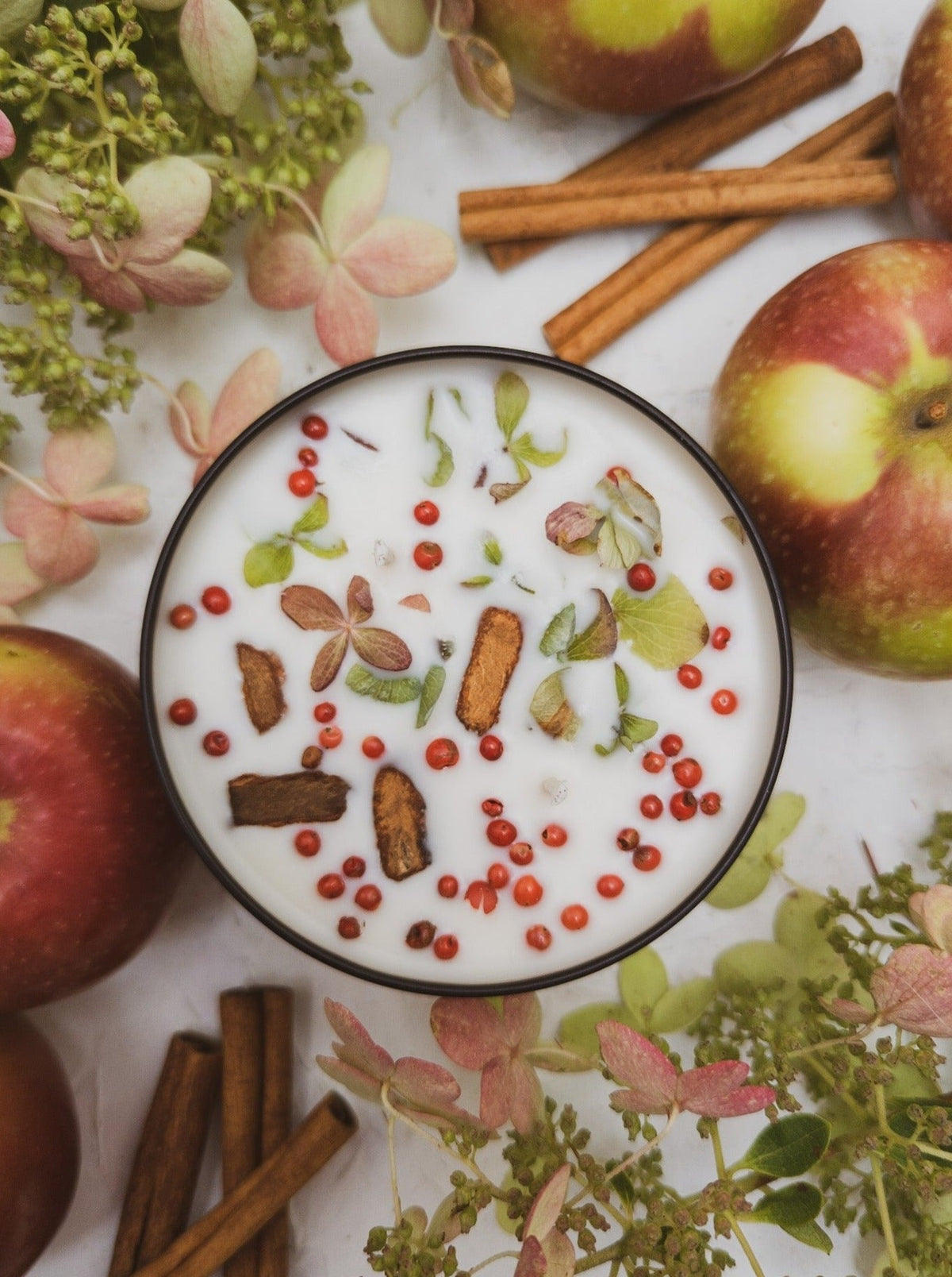 Top of a HARVEST candle tin with cinnamon bark, pink peppercorns and dried hydrangea petals
