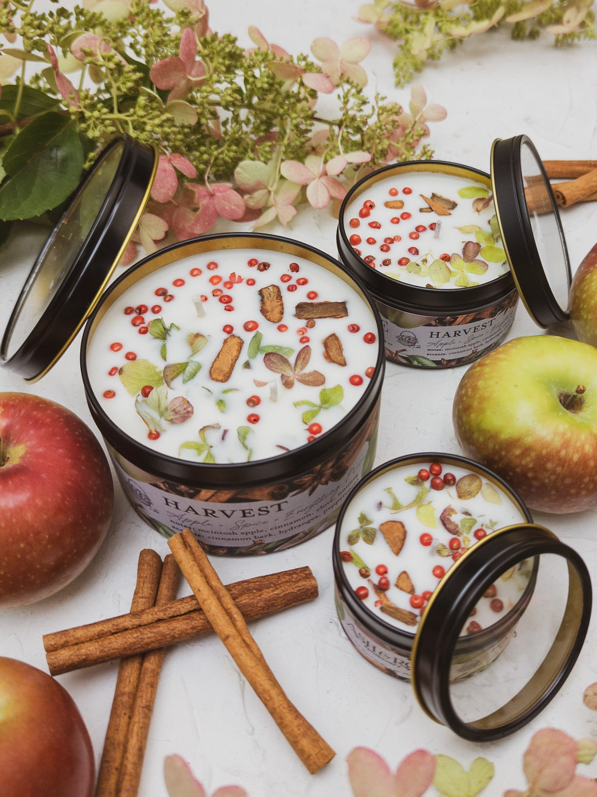 HARVEST candle tins in three sizes with their lids off, among apples and cinnamon sticks