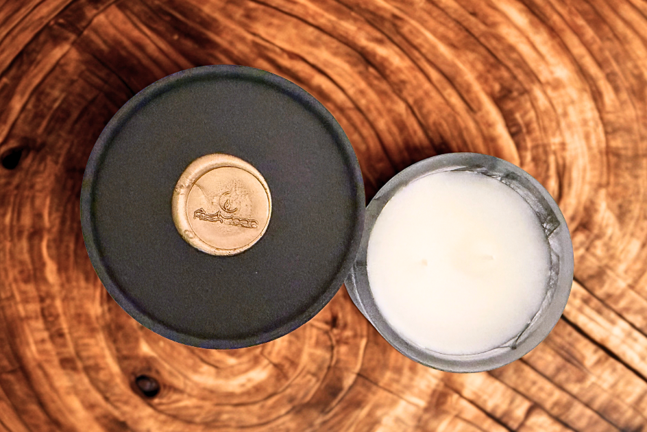 Black lid with a gold seal beside the open candle on a wood slice