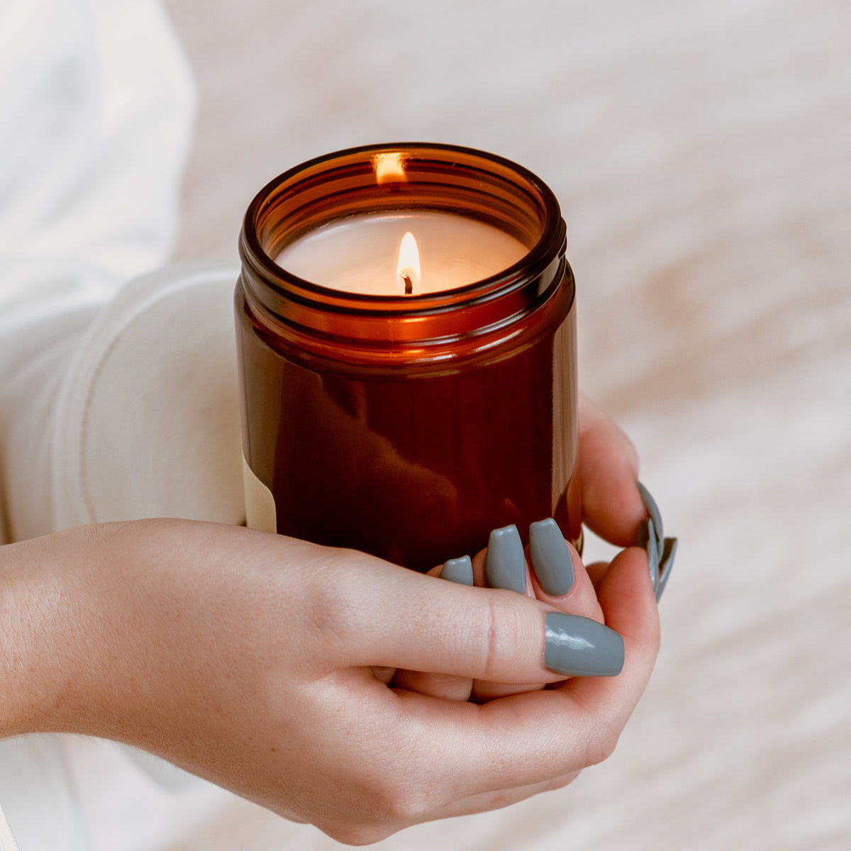 Hands holding a lit Fall Vibe Classic candle