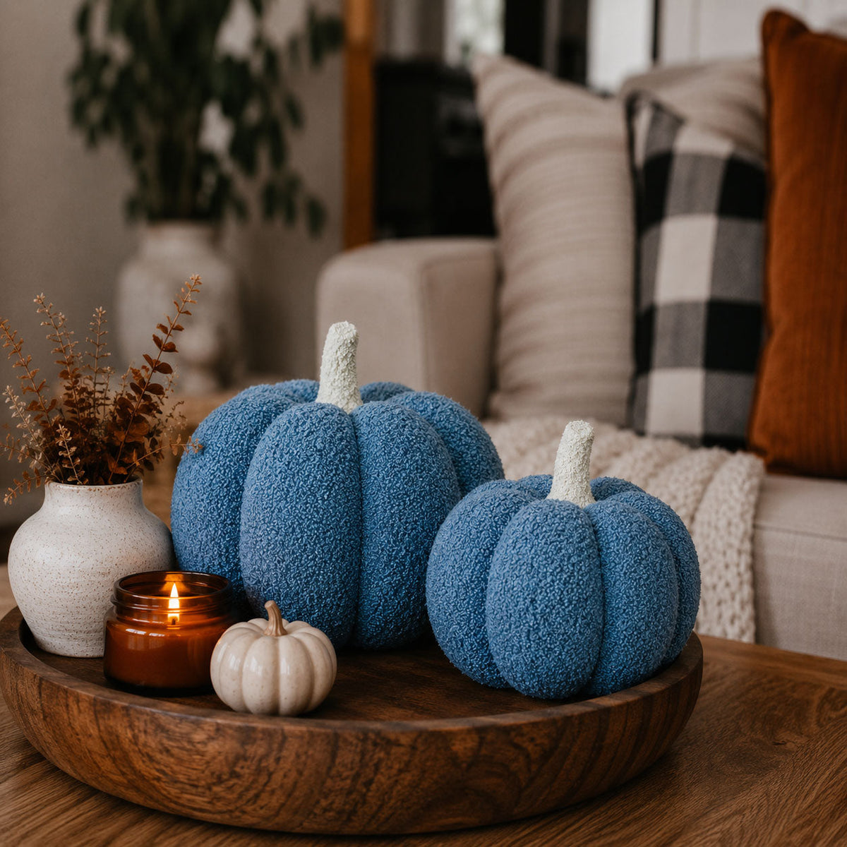 Two blue plush pumpkins on a wooden tray with a lit candle