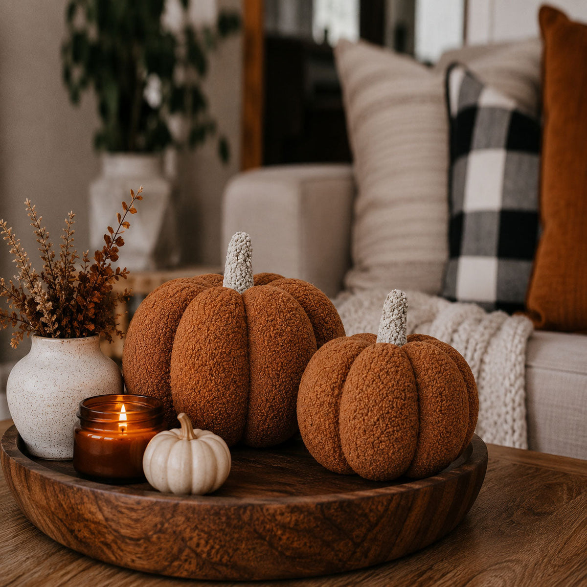 Two brown plush pumpkins on a wooden tray with a lit candle