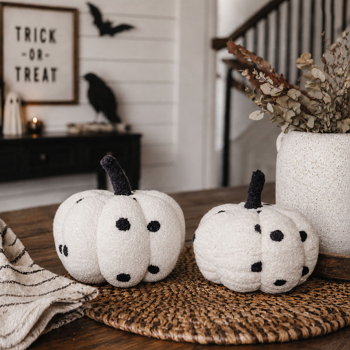 Two black-and-white polka dot plush pumpkins on a woven placemat