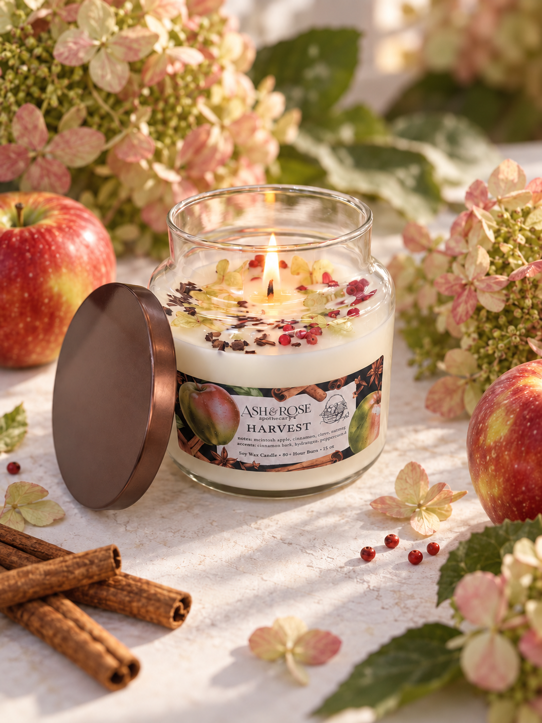 Lit HARVEST apple spice candle in a glass apothecary jar with apples and hydrangeas
