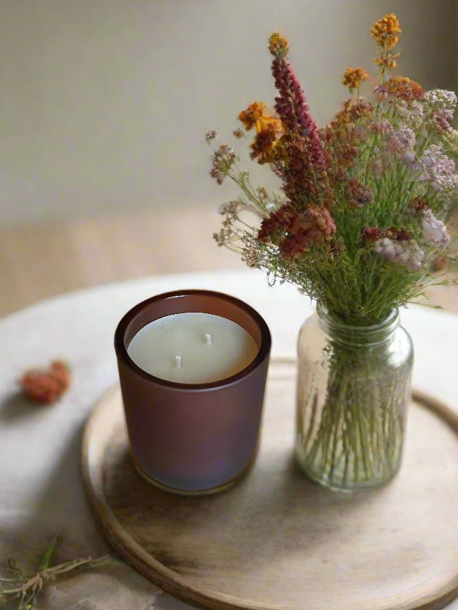 Frosted amber Pumpkin Pie candle on a wooden tray beside a jar of dried flowers