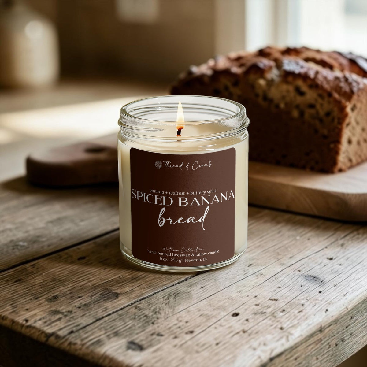 Lit Spiced Banana Bread candle beside a loaf of banana bread on a wooden table