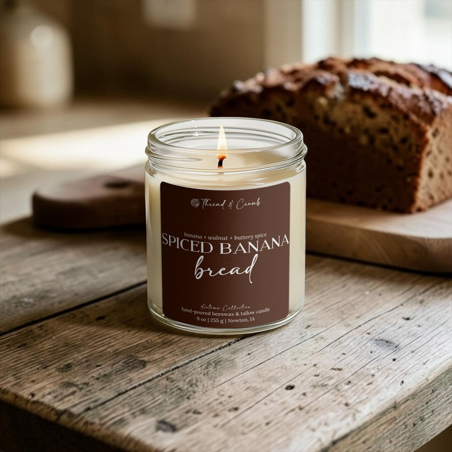 Lit Spiced Banana Bread candle beside a loaf of banana bread on a wooden table