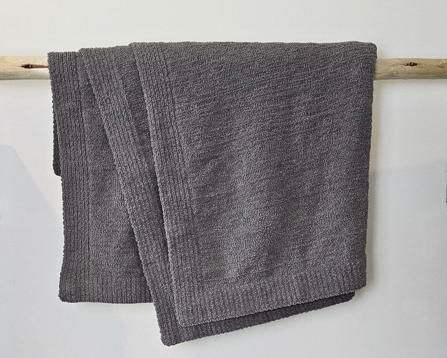 The Nest Throw in Charcoal hanging over a wooden rail